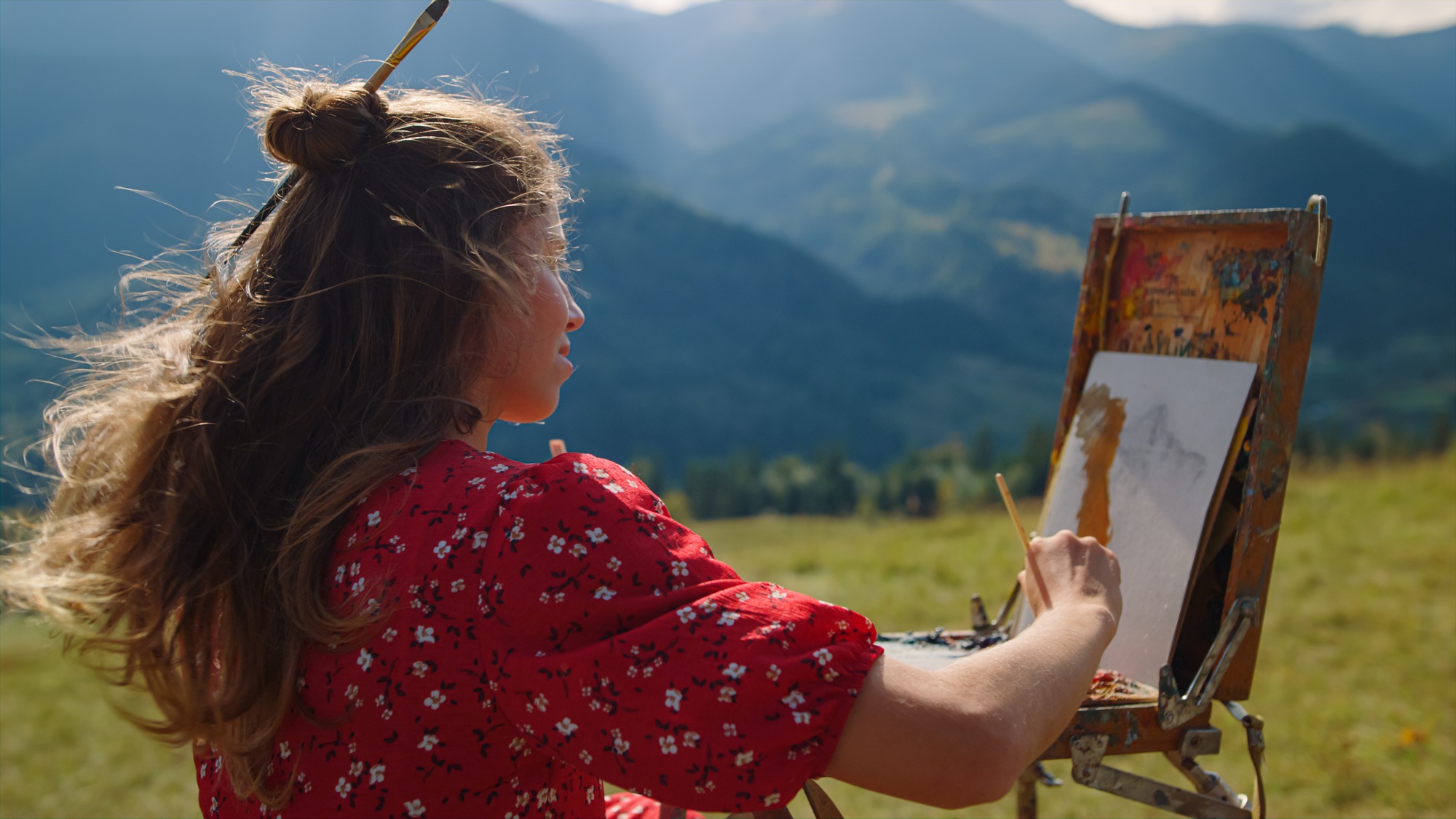 Woman painter drawing mountains landscape on meadow. Girl painting using easel.