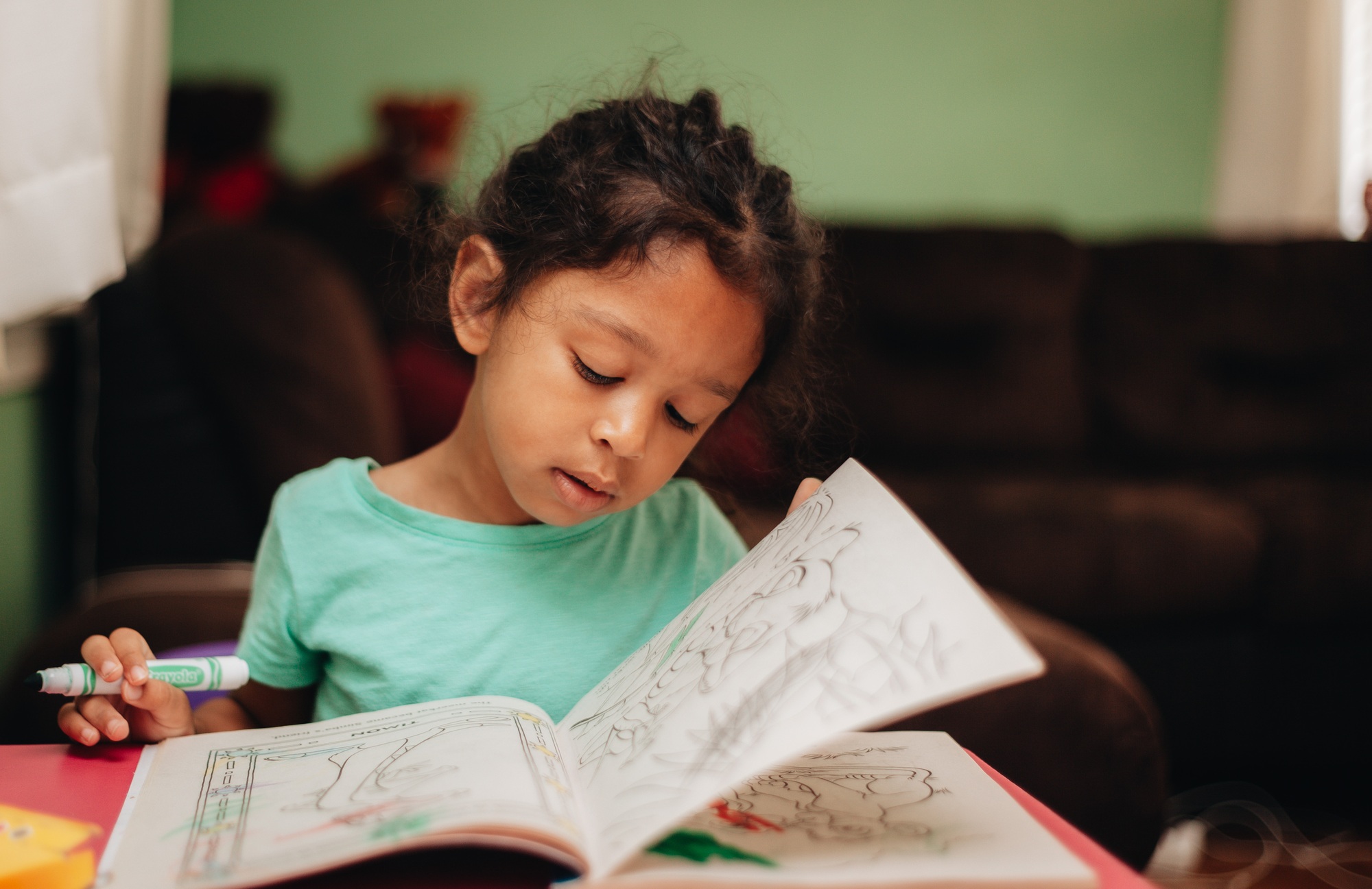 3 year old girl at a desk at home coloring in coloring book, flipping pages