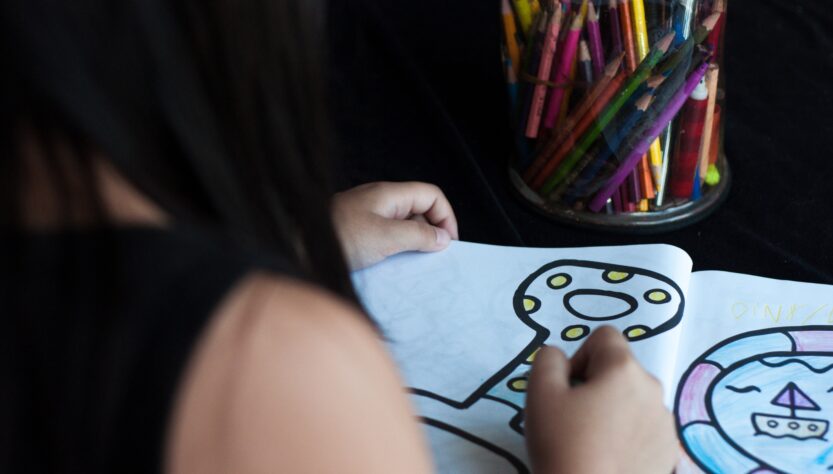 child is colouring a page in the book, view from behind