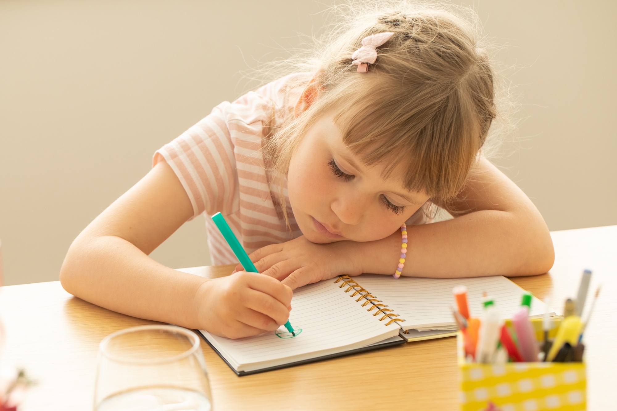 Cute little girl draws picture on notepad page at table